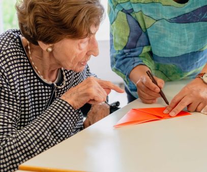 Eine ältere Dame beobachtet eine Falttechnik, die ihr gezeigt wird
