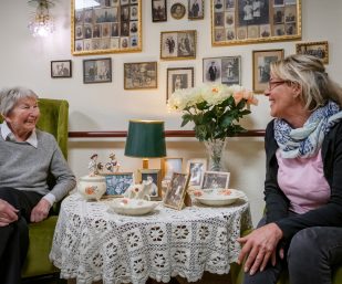 Eine Dame unterhält sich mit ihrer Pflegerin beim Kaffee trinken