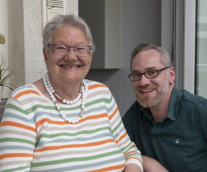 Ältere Dame sitzt draussen lachend mit ihrem Pfleger 